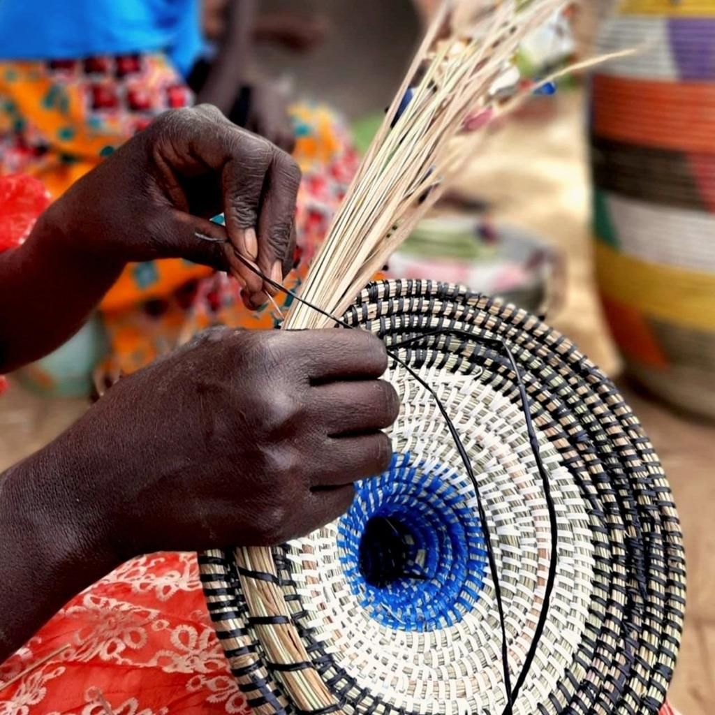 Mains d'une artisane sénégalaise tressant un panier traditionnel coloré